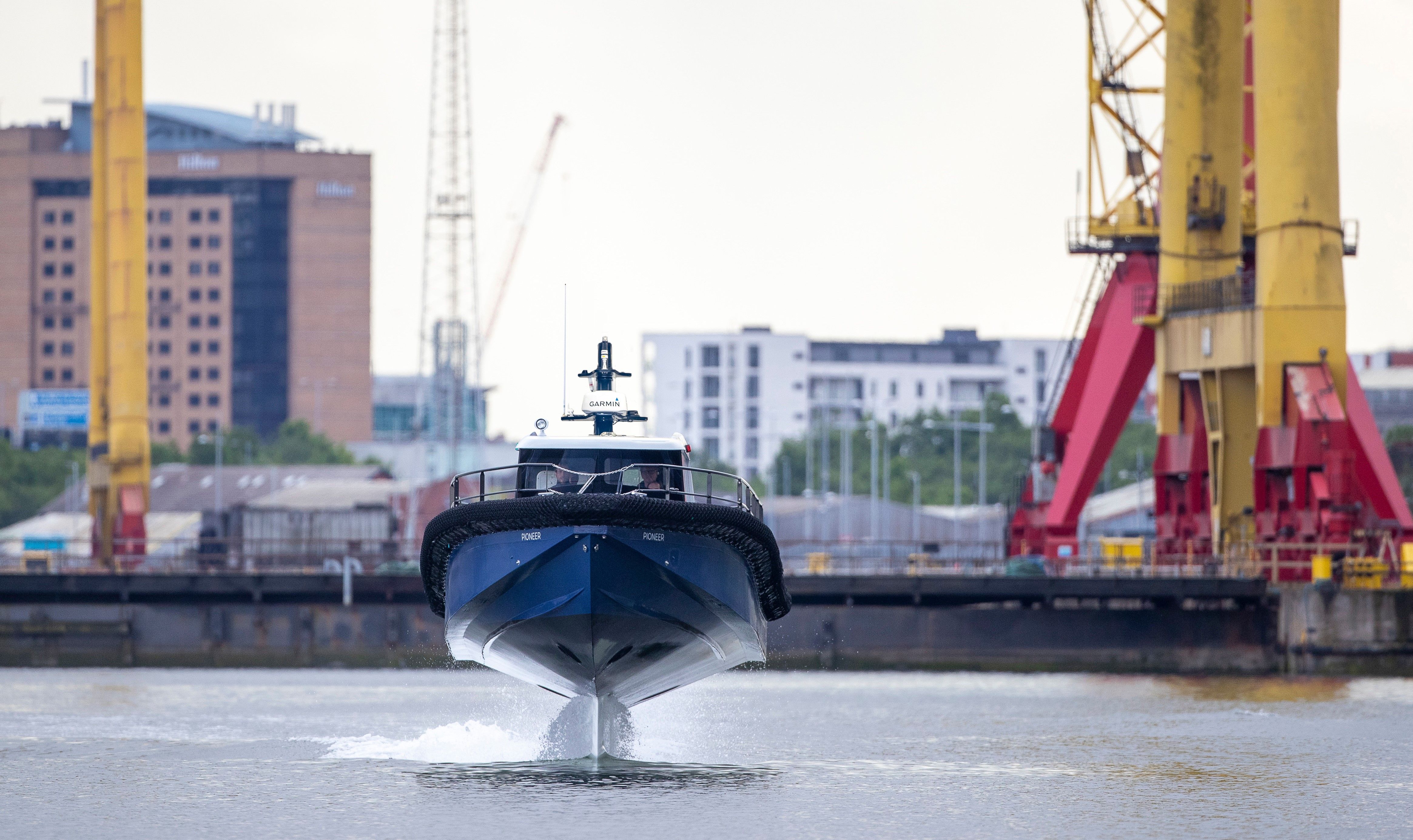 A blue Artemis EF-12 Workboat foiling in Belfast harbour with the feet of the Harland and Wolff cranes in the background