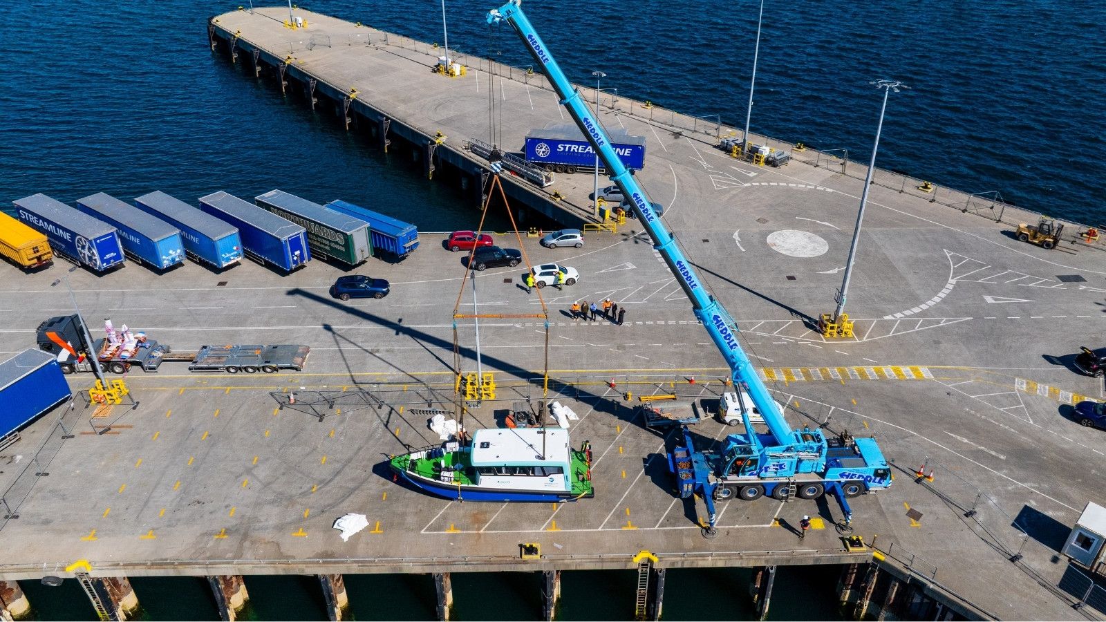 Vessel on pier in Orkney with a blue crane. The vessel has a white body a blue hull and a green deck. It is a sunny day.