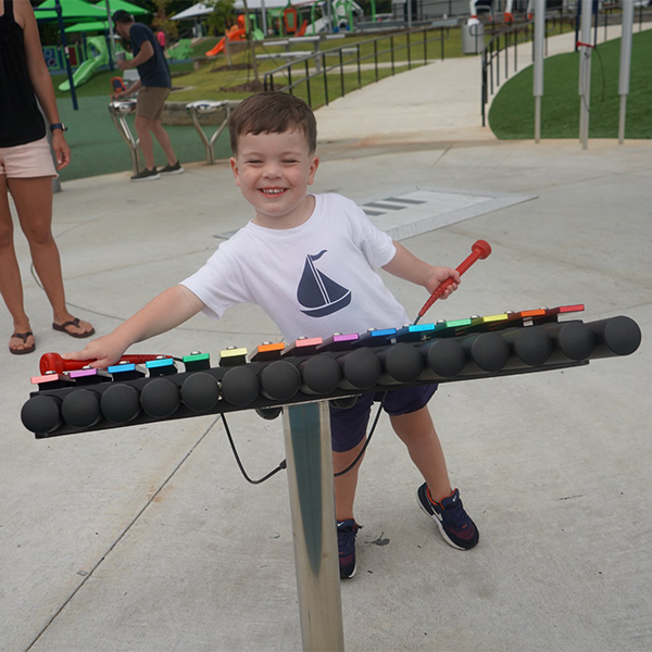 a young boy in shorts and t shirt playing a large outdoor xylophone in an inclusive park