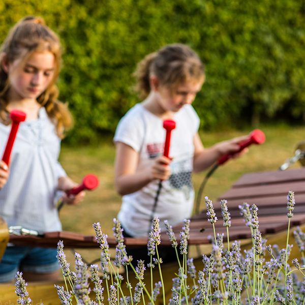 two girls playing a large outdoor marimba in a garden with lavender in the foreground