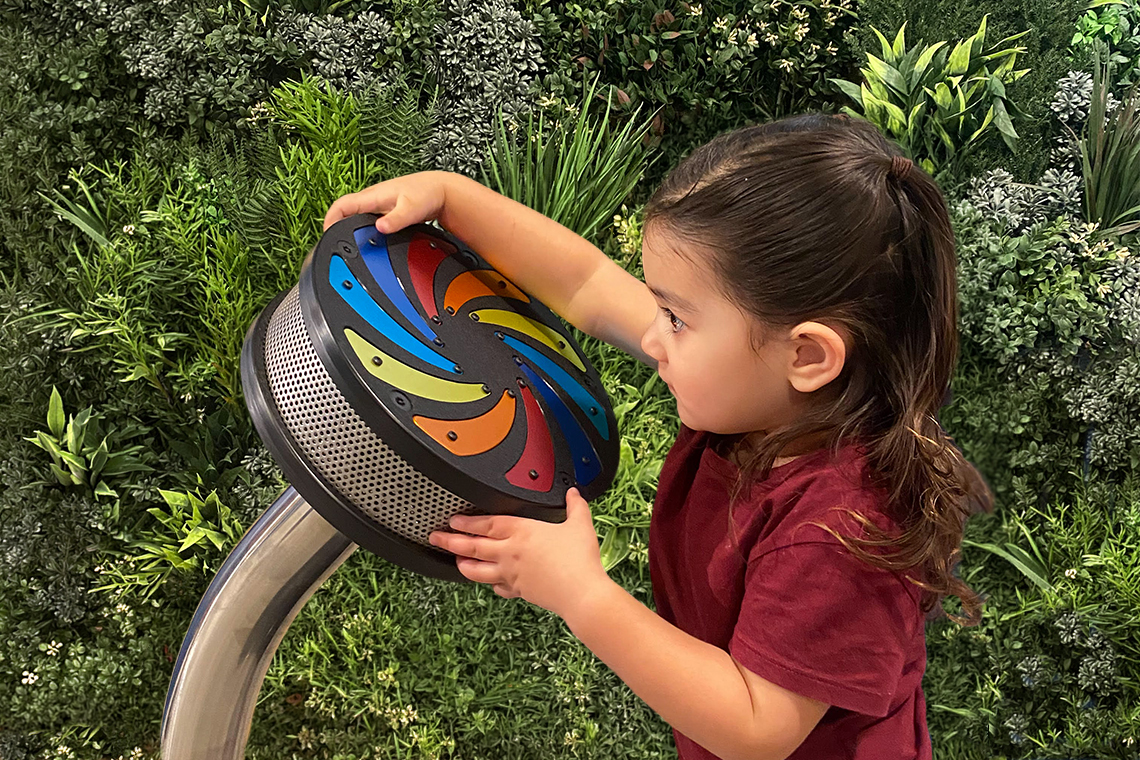 A young girl spinning a circular rainwheel that has rainbow streaks across the center