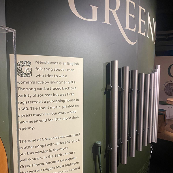A museum display about "Greensleeves," an English folk song, with a description panel and aluminium chimes mounted on a green wall.