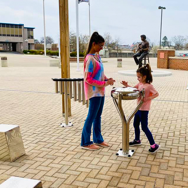 A woman and a child joyfully play a stainless steel tongue drum at the Bill Withers Memorial Plaza's outdoor musical instruments.