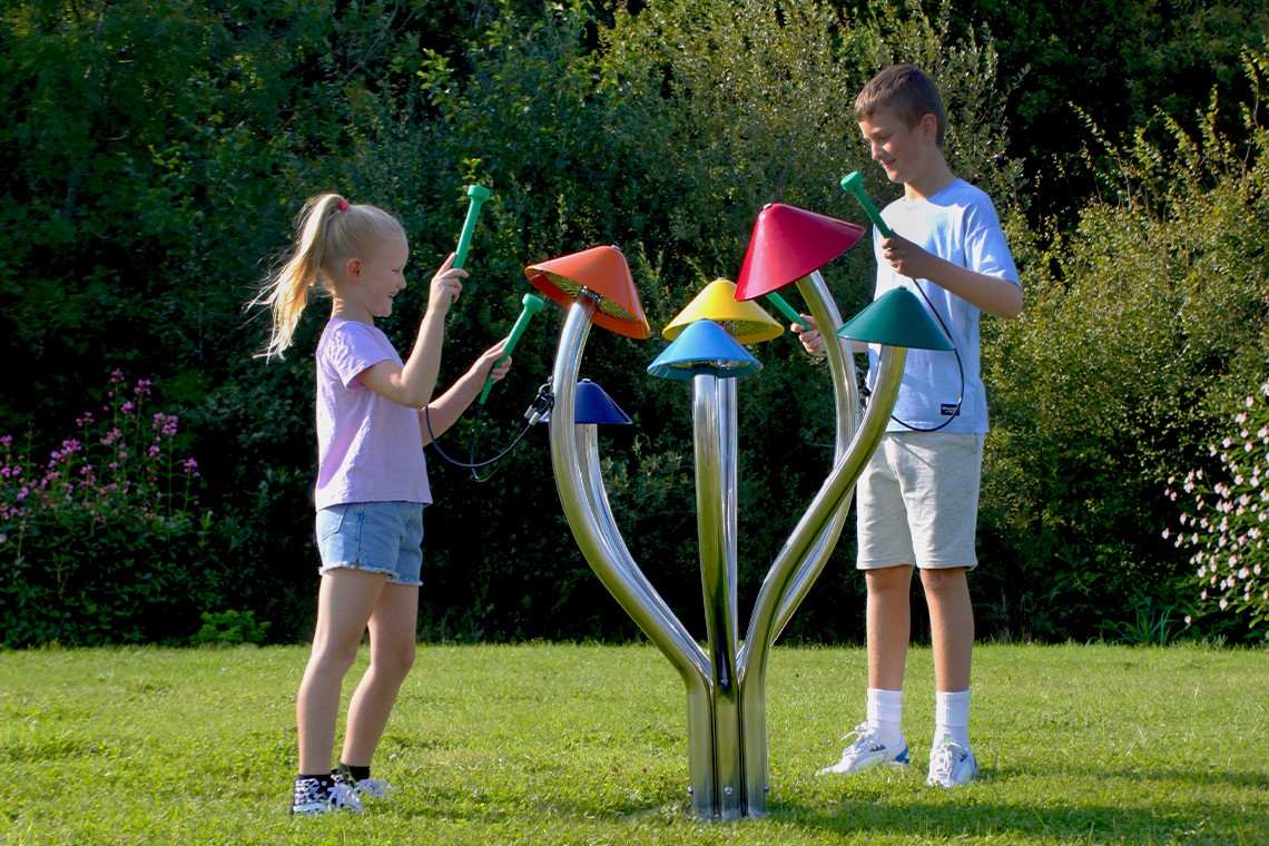 a tall teenage boy and yonger girl playing a large outdoor musical instrument in a park that resembles a group of field mushrooms