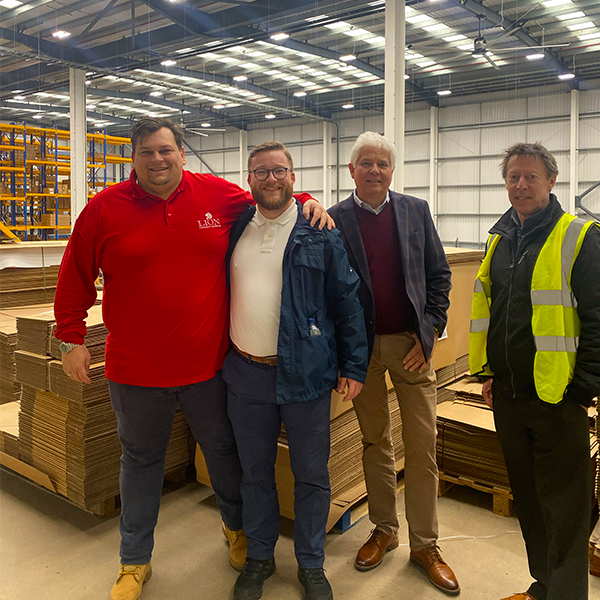 Four men in casual clothing, one in a hi vis, standing on the Percussion Play workshop mezzanine with the workshop and racking behind