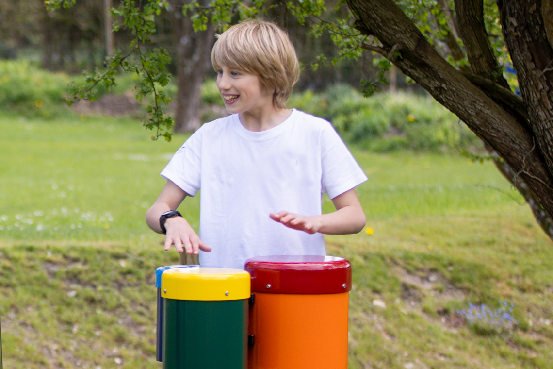 Boy playing rainbow coloured outdoor bongo drums in outdoor space