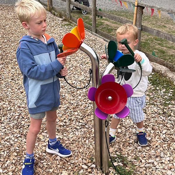 two boys standing in a musical playground playing an outdoor musical instrument shaped liked a flower