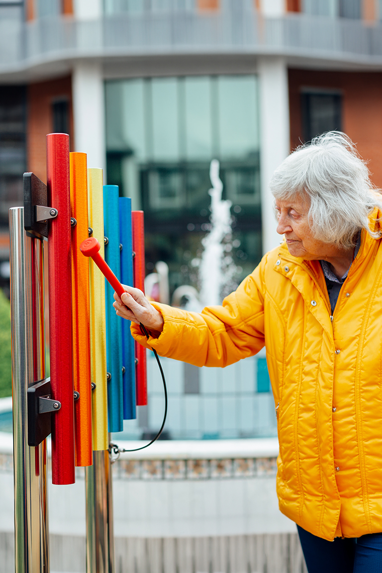 senior lady playing rainbow colored chimes in a courtyard of a senior living environment