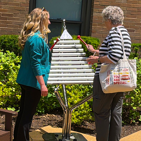two ladies in a care home garden standing and playing a large outdoor musical instrument together