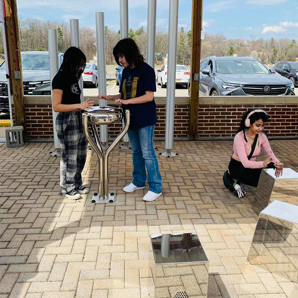 At the Bill Withers Memorial Plaza, three individuals relax on a brick patio playing outdoor musical instruments.