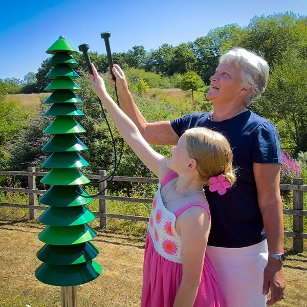 grandmother and granddaughter playing on a large outdoor bell tree in a senior living garden