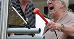two senior ladys one holding a red mallet playing an outdoor metallophone and laughing