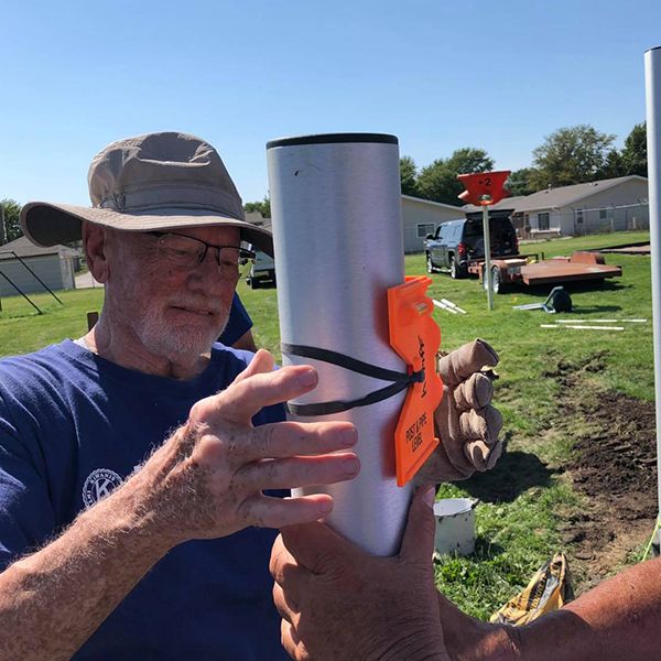 man from the Kiwanis organisation installing a large silver tubular bell in an outdoor musical playground