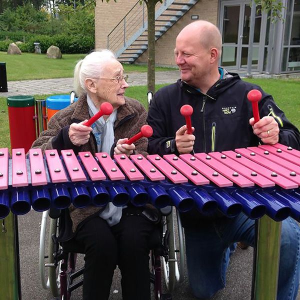 old lady and carer playing outdoor musical instrument together