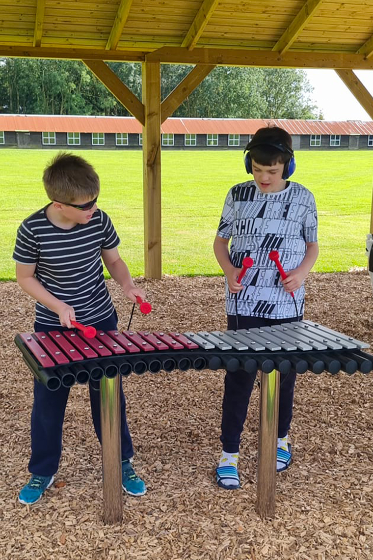 Two boys with autism playing an outdoor xylophone in a music barn
