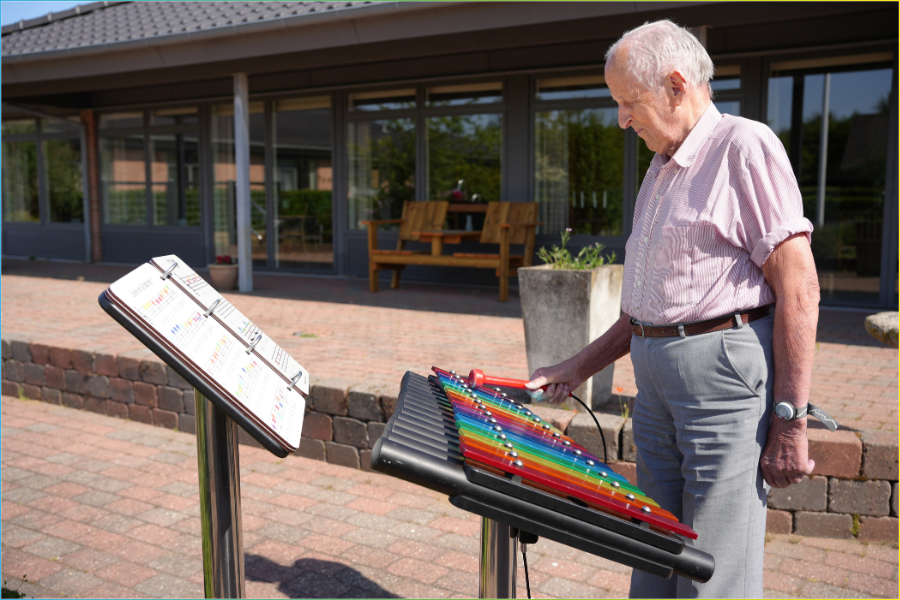 male senior engaging with an outdoor musical instruments in a dementia‑friendly courtyard garden