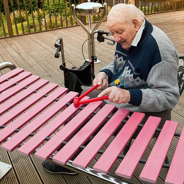 Older man playing an outdoor xylophone in care home garden