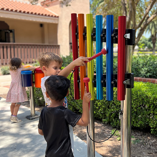 two young boys playing on a set of rainbow colored outdoor musical chimes in a museum garden
