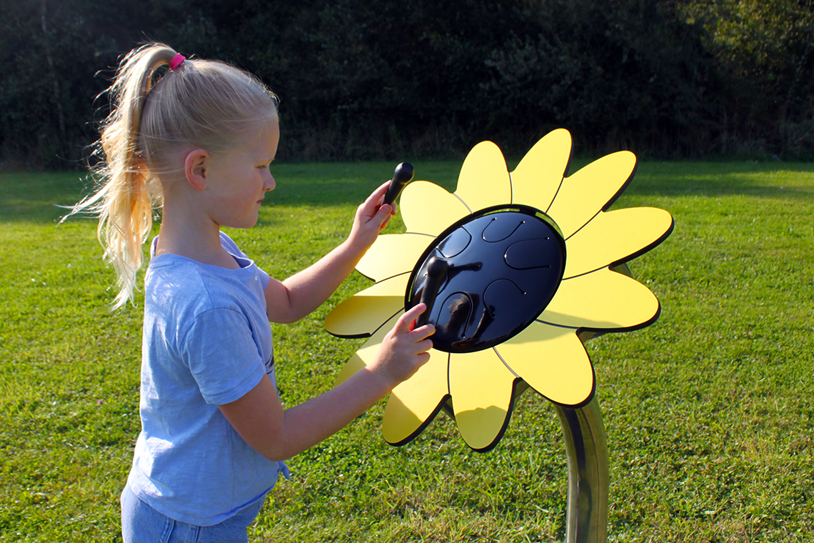 young girl with a pony tail playing an outdoor musical drum that looks like a sunflower