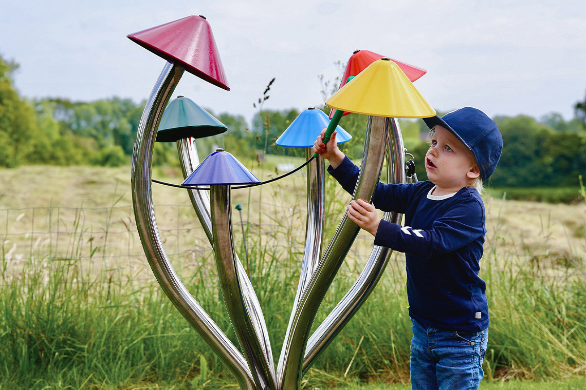 a young boy playing a large colorful outdoor musical instrument that resembles field mushrooms