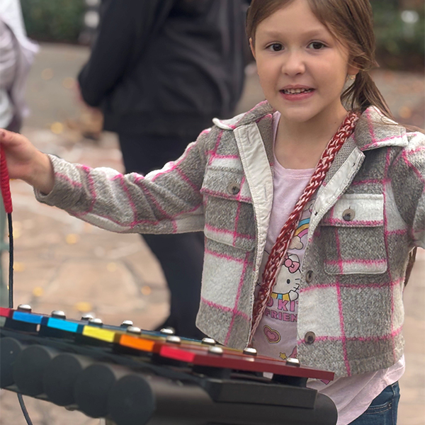 a young girl playing on a rainbow colored xylophone outdoor musical instrument in a childrens museum garden