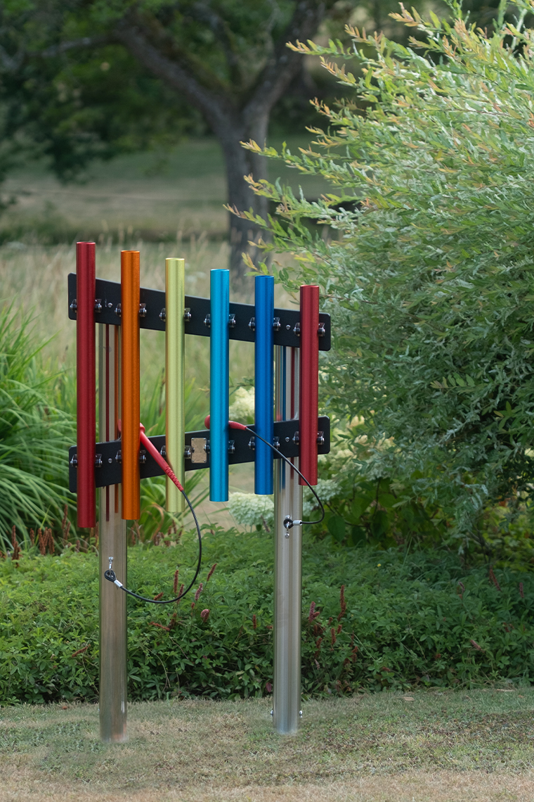 a set of outdoor rainbow chimes with red mallets in a summer garden