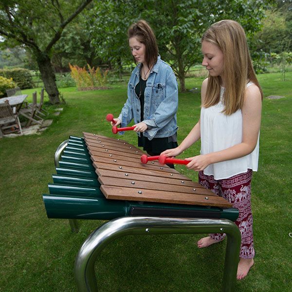 side view of two teenage girls playing a large marimba made of timber notes and metal frame in a park