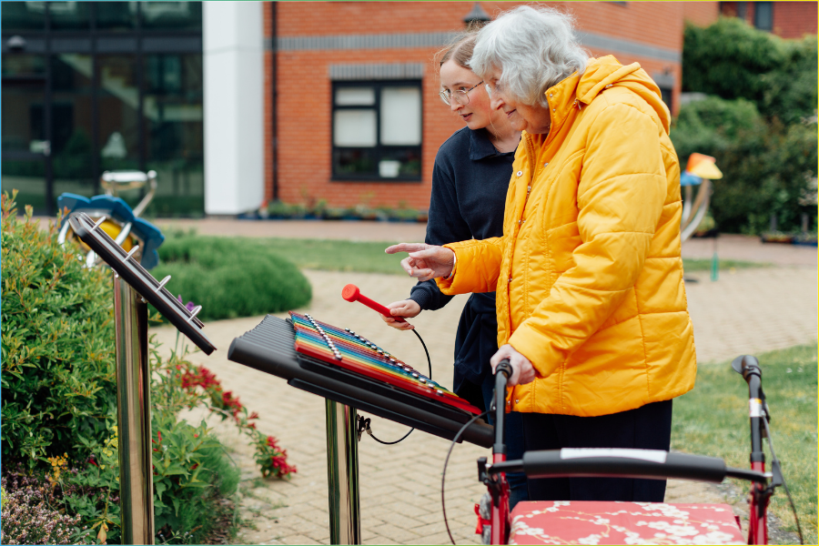 Resident and carer sharing a musical moment using outdoor instruments in a dementia‑friendly garden