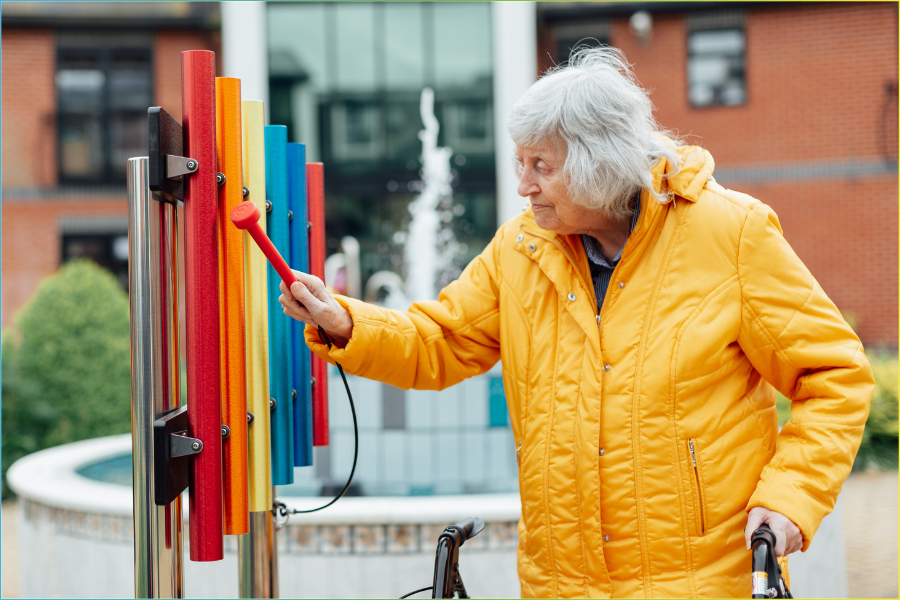 Senior lady playing an outdoor musical instrument in a sound garden within a care home setting