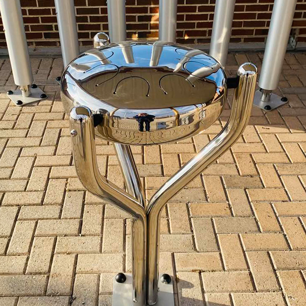A metal outdoor tongue drum at the Bill Withers Memorial Plaza, reflecting the environment in its shiny stainless steel surface.