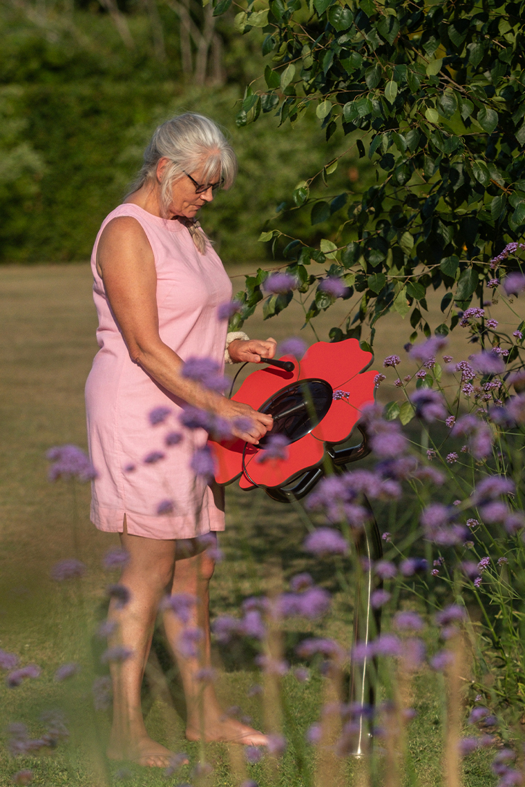 a lady in a pink dress playing an outdoor drum that resembles a poppy in a garden