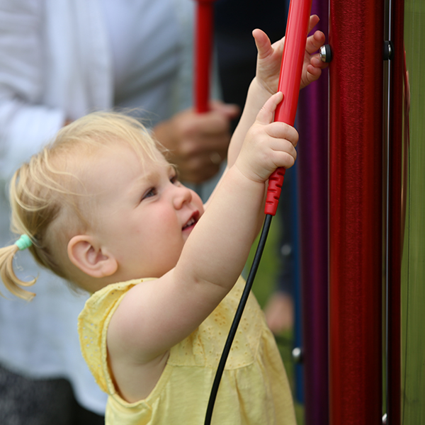 a young girl playing on a red chime in a musical playground