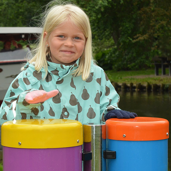 a young blonde girl playing a colourful pair of outdoor conga drums in a musical playground