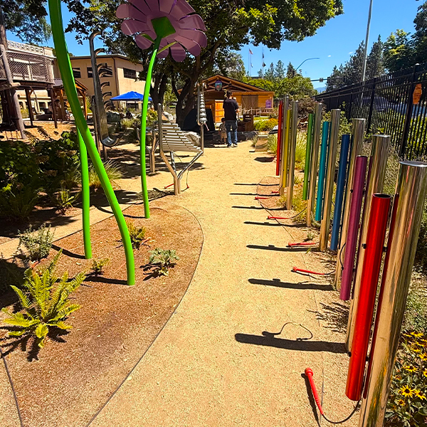 rainbow colored outdoo musical chimes alongside other outdoor musical instruments in a music garden