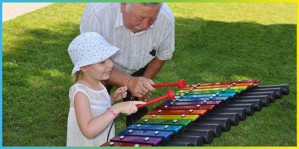 grandfather playing large outdoor xylophone in a music park with grandaughter
