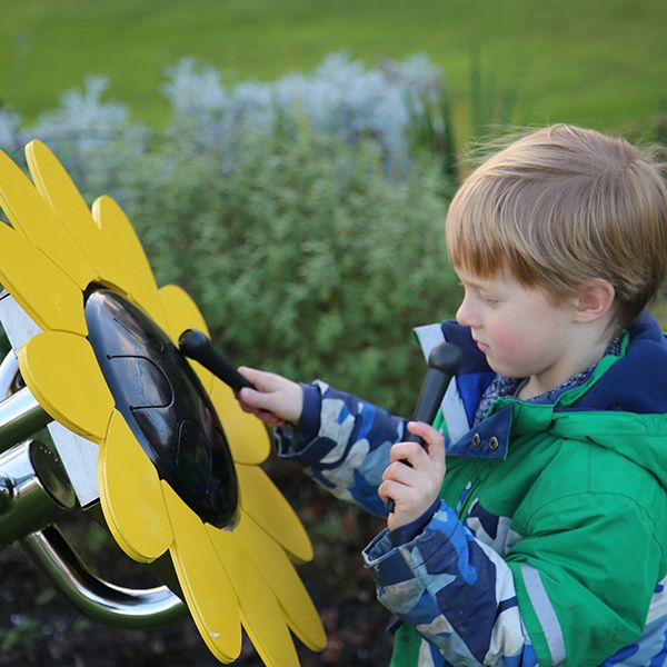 A young boy playing an outdoor musical drum in the shape and colours of a sunflower