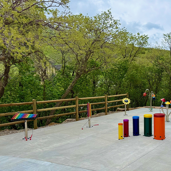 a collection of colorful outdoor musical instruments on a playground surrounded by trees