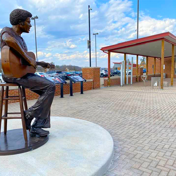 Statue of Bill Withers sitting on a stool with a guitar, located at the Bill Withers Memorial Plaza among outdoor instruments.