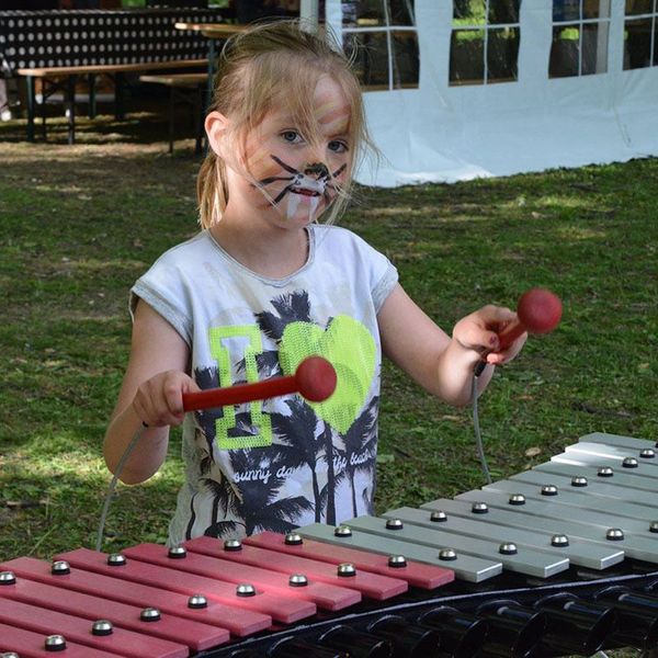 Young girl with her face painted playing a large outdoor xylophone in the park