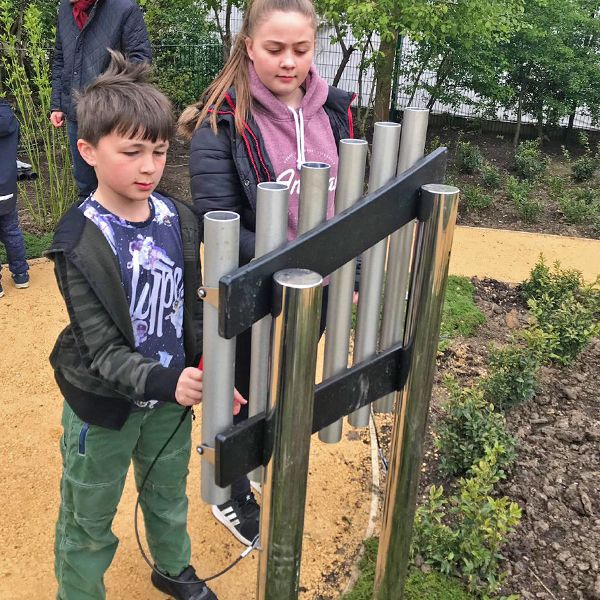 a boy and a girl playing outdoor musical chimes in the paddington recreation ground sensory trail