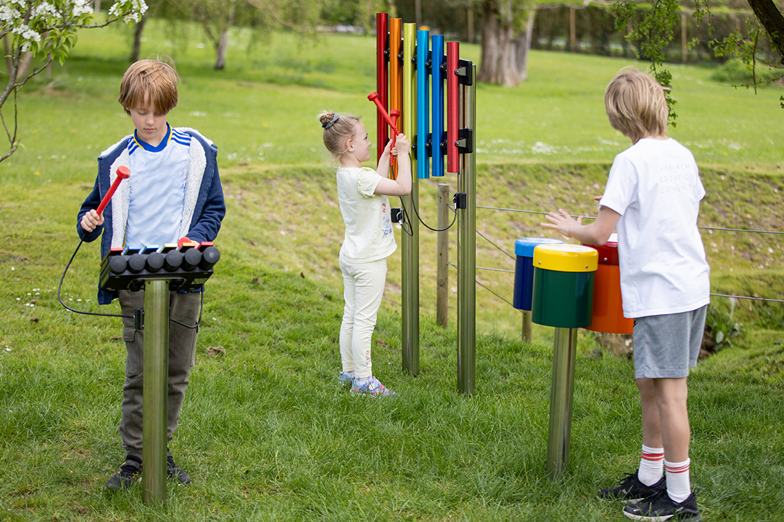 Group of children playing on rainbow coloured instruments outdoors
