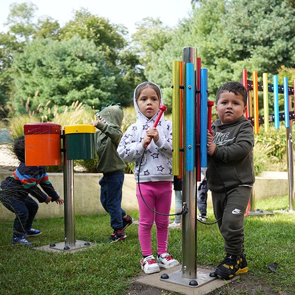 Two young children playing an outdoor musical chime post 
