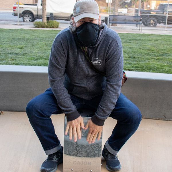 a man wearing a face mask playing an outdoor cajon drum at the gallo center music garden