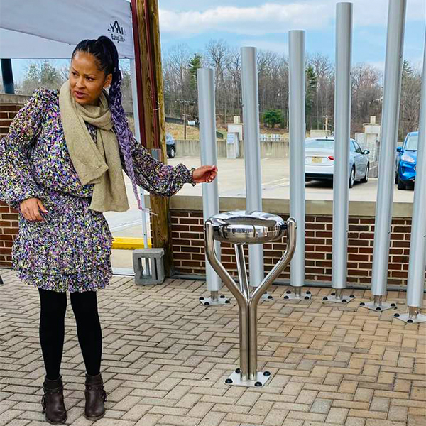 At the Bill Withers Memorial Plaza, a woman stands next to a stainless steel outdoor drum with  tall outdoor musical chimes behind her