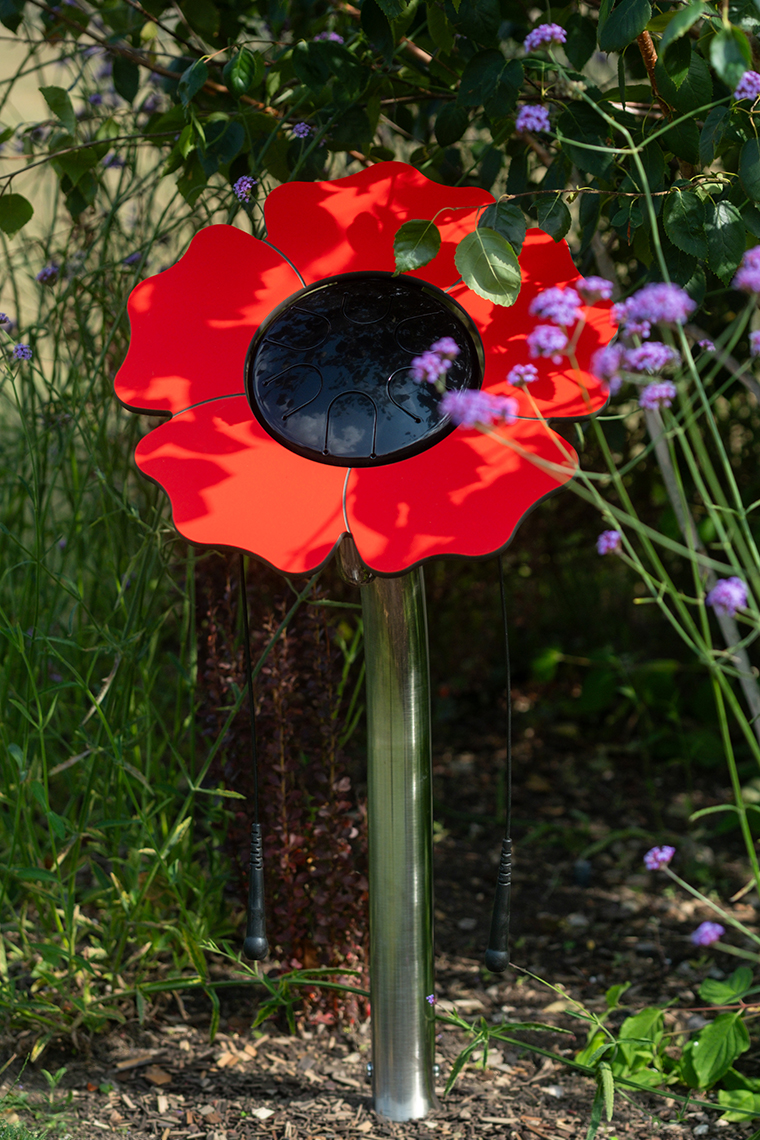 a black outdoor tongue drum with a red petal shaped surround made to resemble a poppy